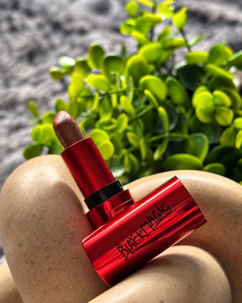 An open Black Magic lipstick, with a plant behind it